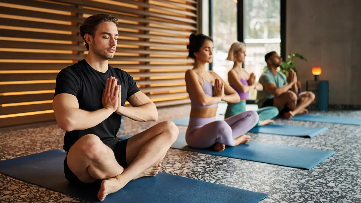 A group of people are sitting on yoga mats with their hands folded.