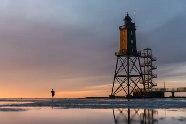 A person is walking along the beach next to the Obereversand lighthouse.