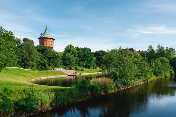A waterway lined with trees, with the water tower in Cuxhaven in the background.
