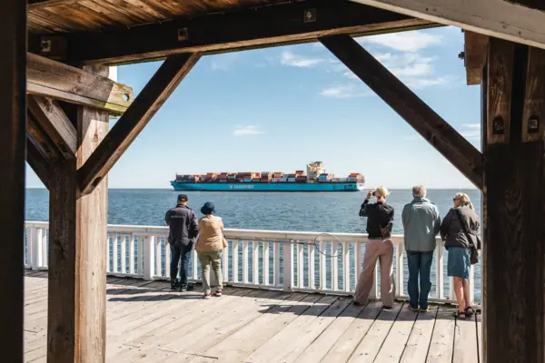 A group of people are looking at a large ship from the ‘Alte Liebe’ viewing platform in Cuxhaven.