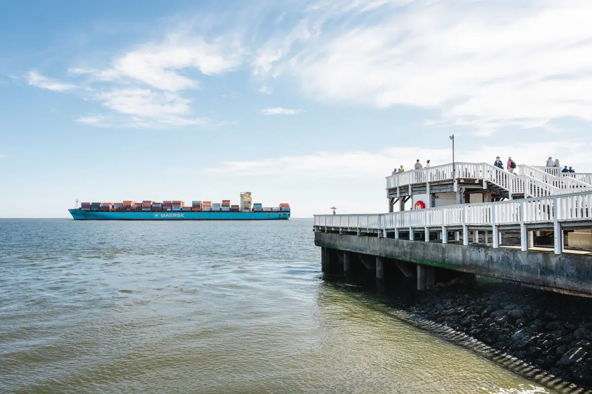 A container ship is sailing in the water in front of a jetty.